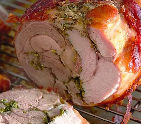 Sliced tuscan-style turkey alla porchetta wrapped in prosciutto with fennel and herb crust on a cutting board