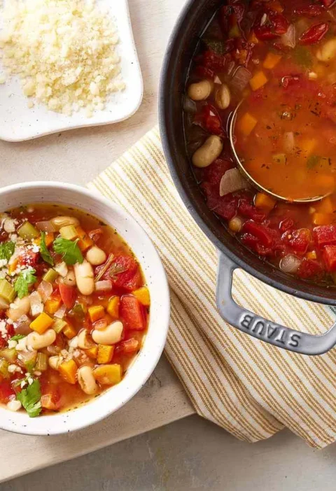 A warm bowl of vegetable bean soup with cannellini beans, diced tomatoes, and carrots in broth topped with Parmesan