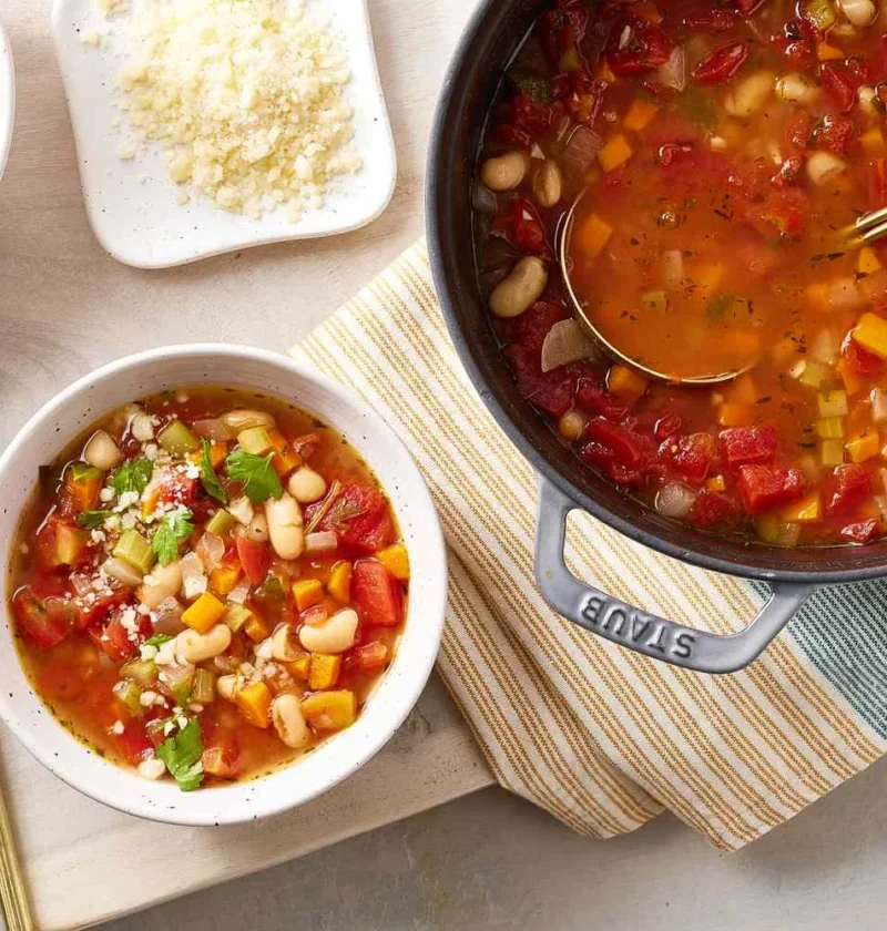 A warm bowl of vegetable bean soup with cannellini beans, diced tomatoes, and carrots in broth topped with Parmesan