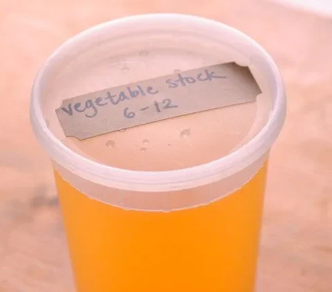 Martha Stewart vegetable stock in a glass jar with fresh herbs and vegetables