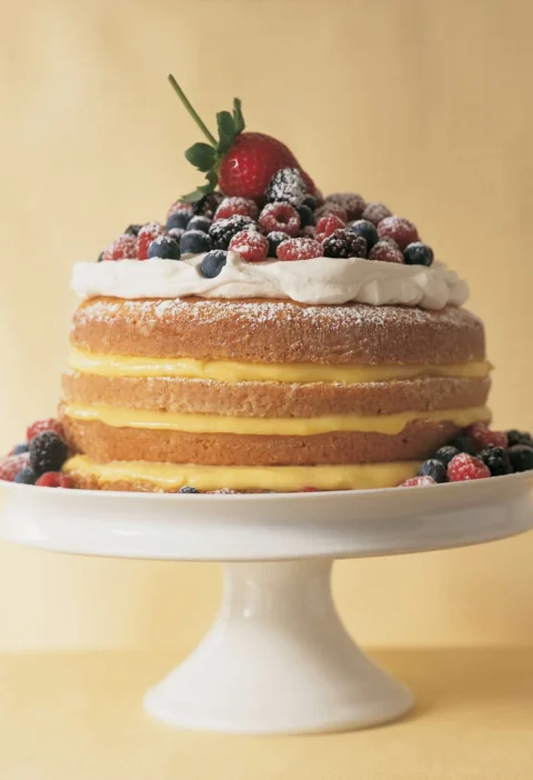 Martha Stewart 1-2-3-4 lemon cake with lemon curd layers, whipped cream and fresh berries on a white cake stand