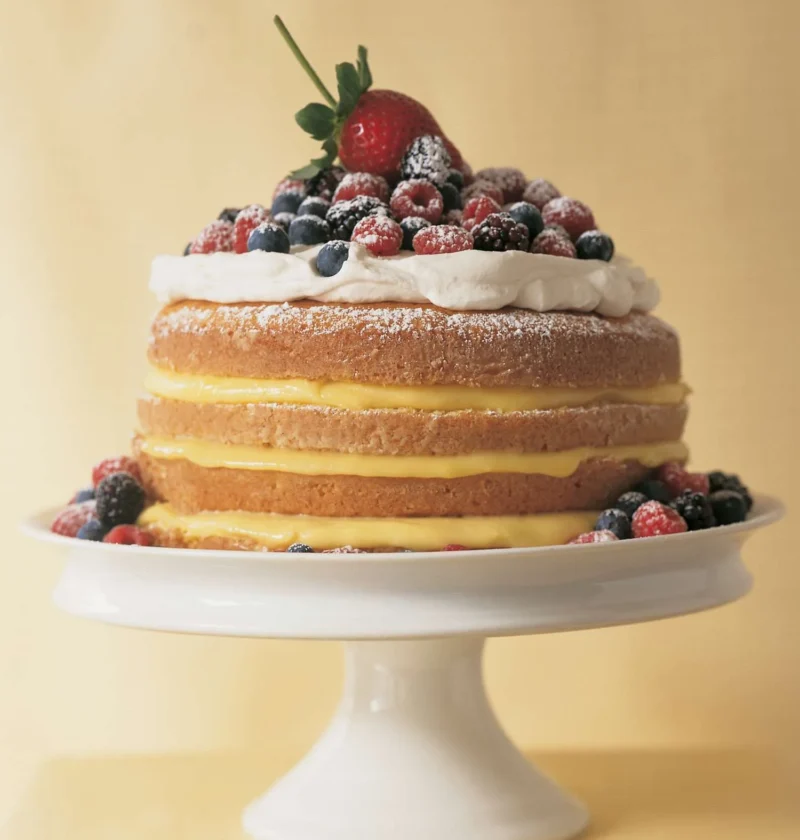 Martha Stewart 1-2-3-4 lemon cake with lemon curd layers, whipped cream and fresh berries on a white cake stand