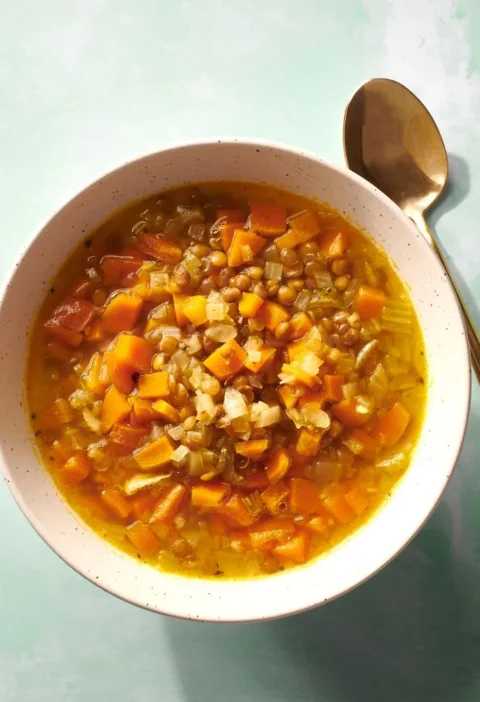 Martha Stewart 15-Minute Lentil Soup with diced carrot, celery and lentils in a speckled bowl with a gold spoon
