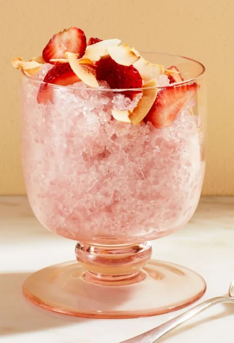 Martha Stewart 2-ingredient coconut granita in a footed pink glass topped with sliced strawberries and toasted coconut flakes