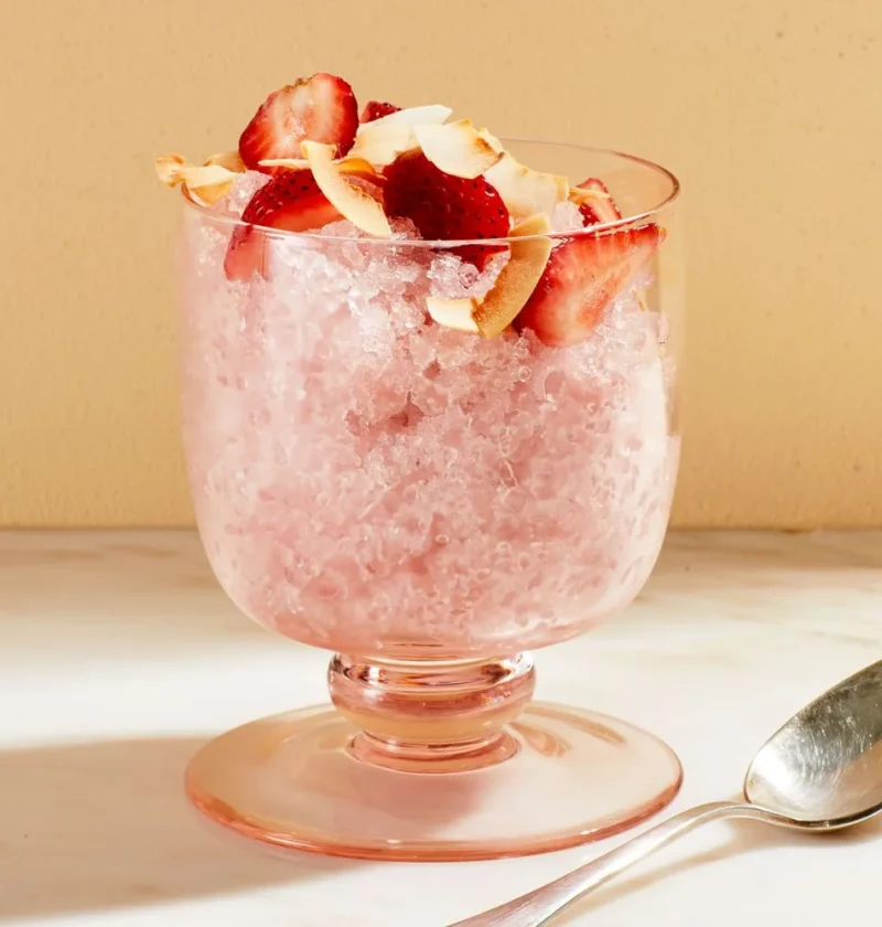Martha Stewart 2-ingredient coconut granita in a footed pink glass topped with sliced strawberries and toasted coconut flakes
