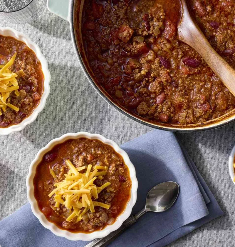 Martha Stewart 30-minute chili topped with shredded cheddar in white bowls next to a Dutch oven of beef and bean chili
