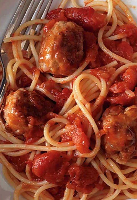 Martha Stewart 30-minute spaghetti and meatballs in a white bowl with chunky tomato sauce and a fork