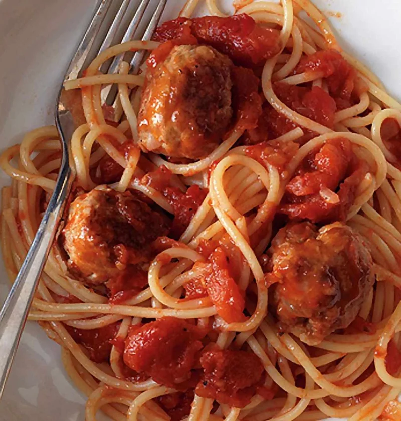 Martha Stewart 30-minute spaghetti and meatballs in a white bowl with chunky tomato sauce and a fork