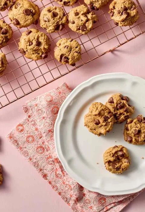 Martha Stewart 5-ingredient chocolate chip cookies cooling on a wire rack and served on a white plate on a pink background
