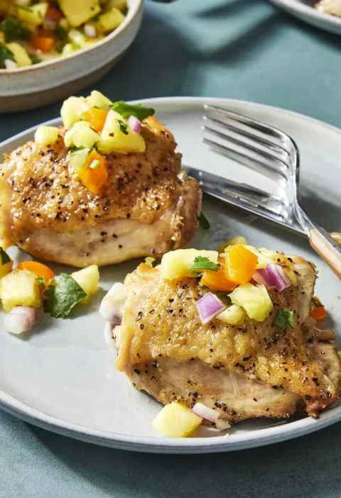 Martha Stewart 5-ingredient pineapple salsa with diced pineapple, red onion and orange bell pepper spooned over seared chicken thighs