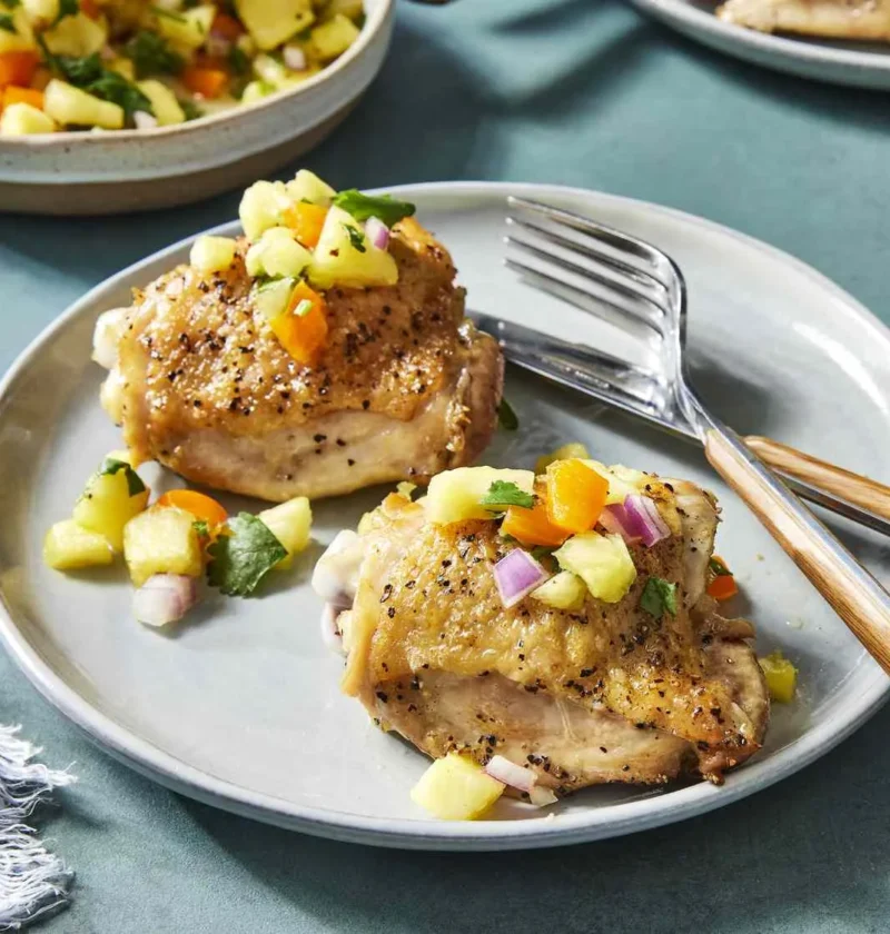 Martha Stewart 5-ingredient pineapple salsa with diced pineapple, red onion and orange bell pepper spooned over seared chicken thighs