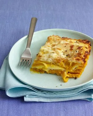 Slice of Martha Stewart acorn squash lasagna with golden Parmesan top on a pale blue plate with a fork