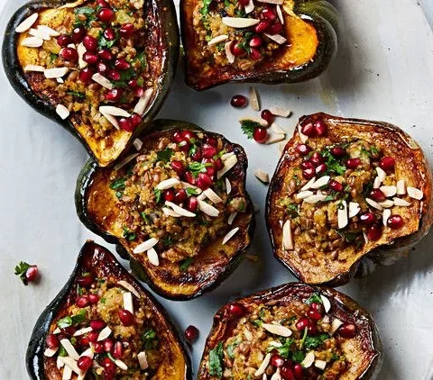 Martha Stewart acorn squash with mixed-grain stuffing topped with pomegranate seeds, slivered almonds and parsley on a platter