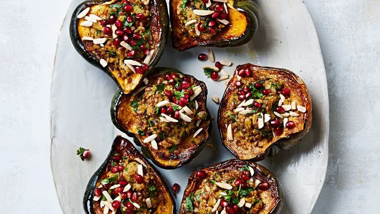 Martha Stewart acorn squash with mixed-grain stuffing topped with pomegranate seeds, slivered almonds and parsley on a platter