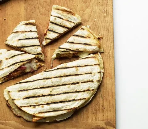 Martha Stewart adobo-marinated chicken quesadillas with grill marks cut into wedges on a wooden cutting board