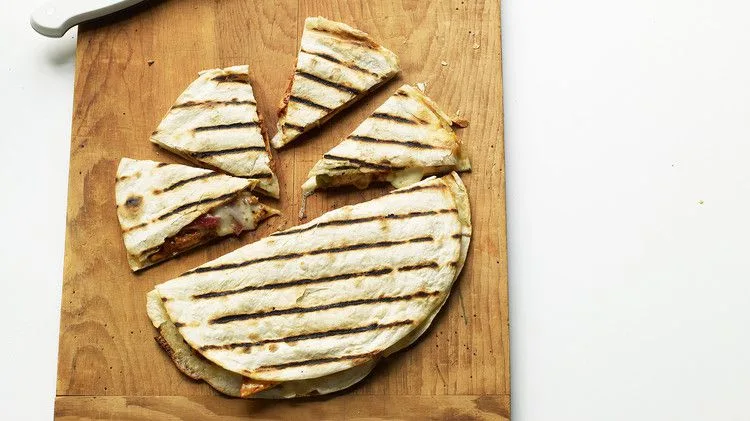 Martha Stewart adobo-marinated chicken quesadillas with grill marks cut into wedges on a wooden cutting board