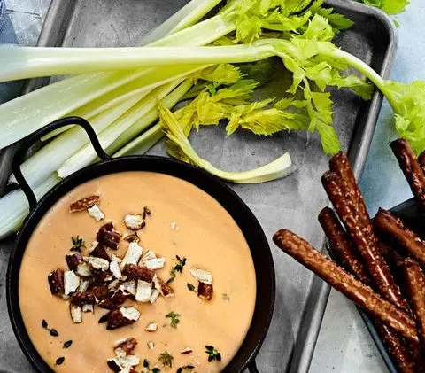Martha Stewart aged-cheddar and beer dip in a black skillet topped with crushed pretzels and thyme, served with celery stalks and pretzel rods