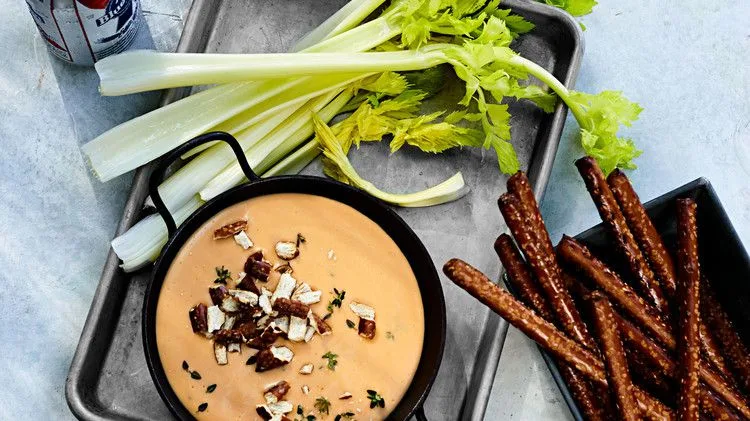 Martha Stewart aged-cheddar and beer dip in a black skillet topped with crushed pretzels and thyme, served with celery stalks and pretzel rods