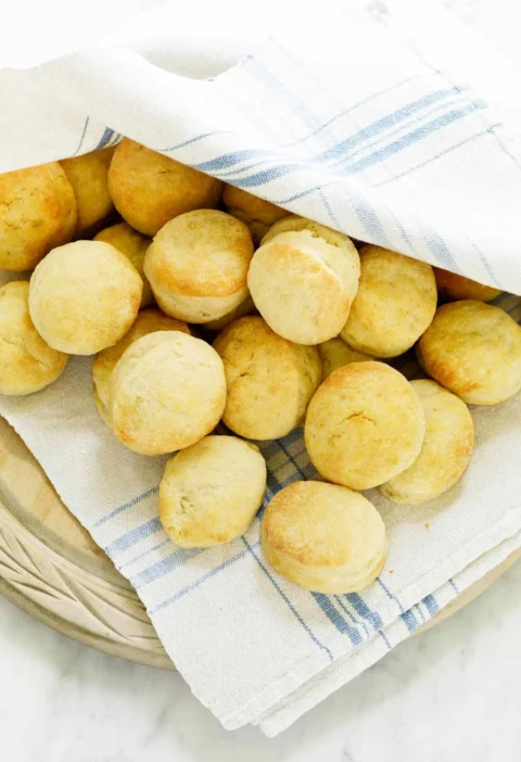 Martha Stewart airy angel biscuits, small golden rounds piled in a bowl lined with a blue-striped kitchen towel