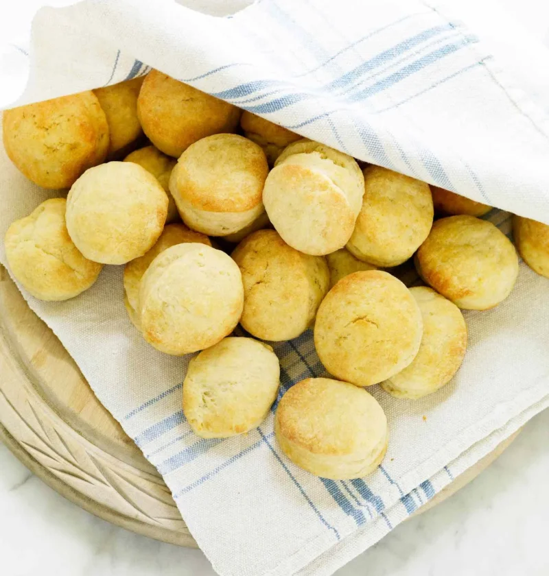Martha Stewart airy angel biscuits, small golden rounds piled in a bowl lined with a blue-striped kitchen towel
