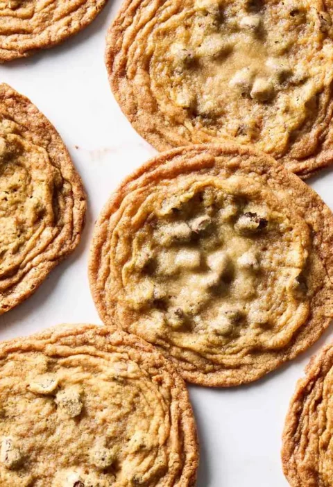 Thin crispy brown sugar chocolate chip cookies with rippled golden edges arranged on a white surface