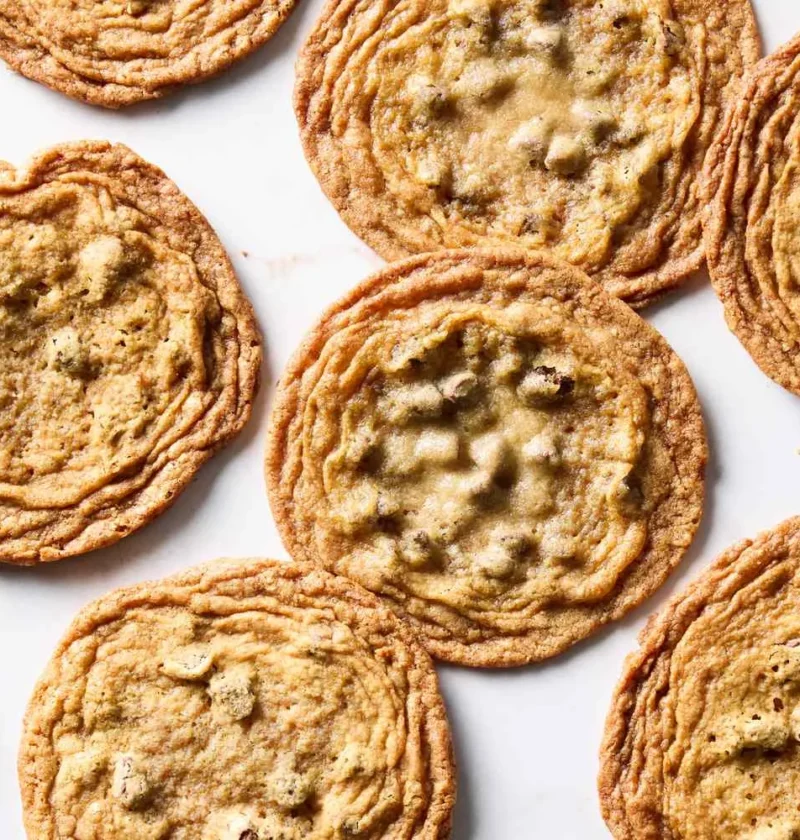 Thin crispy brown sugar chocolate chip cookies with rippled golden edges arranged on a white surface