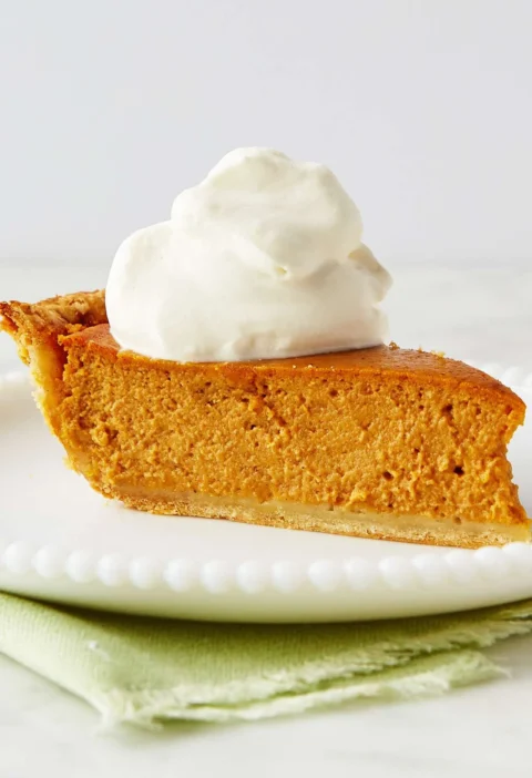 Slice of Martha Stewart Alexis's sweet potato pie topped with whipped cream on a white beaded plate