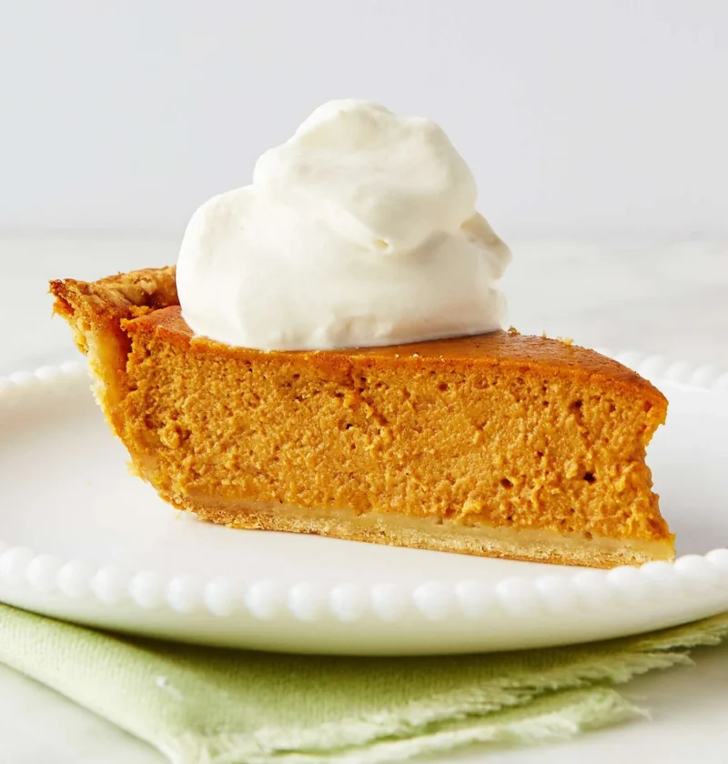 Slice of Martha Stewart Alexis's sweet potato pie topped with whipped cream on a white beaded plate