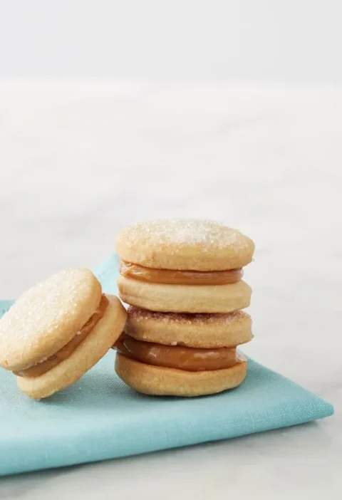Stacked Martha Stewart alfajores de dulce de leche sandwich cookies with sugared tops on a light blue napkin