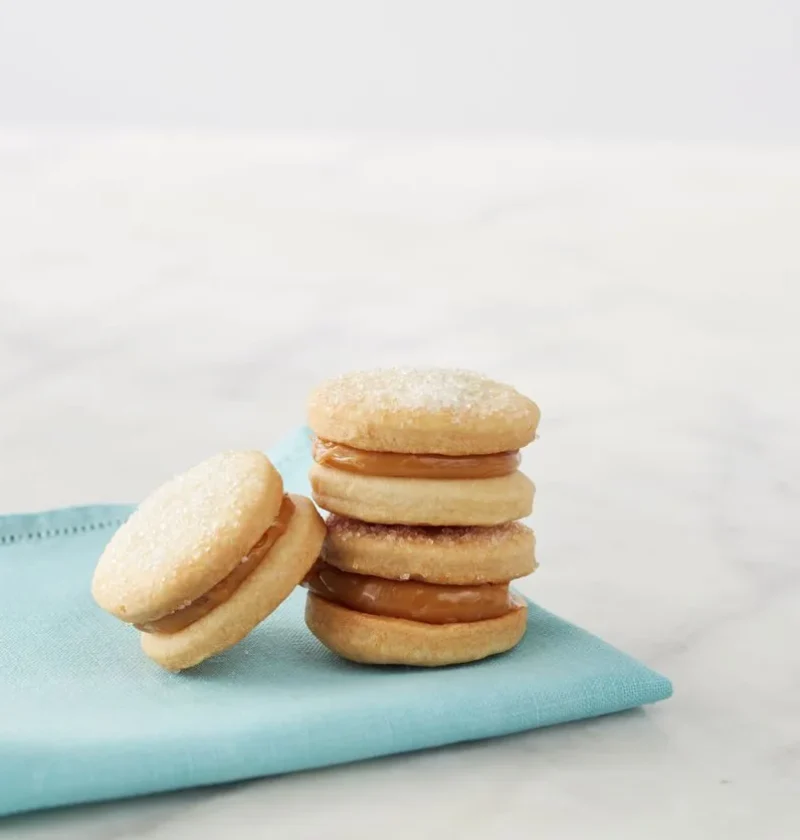Stacked Martha Stewart alfajores de dulce de leche sandwich cookies with sugared tops on a light blue napkin