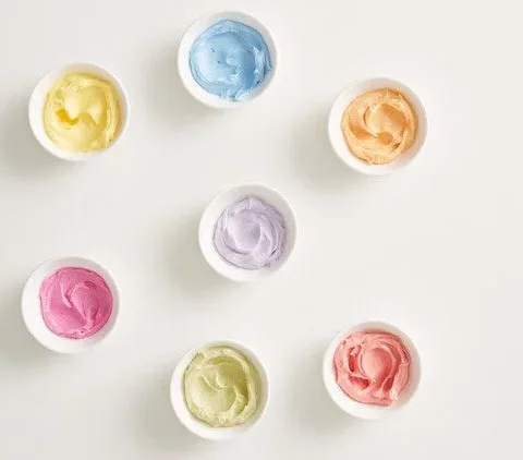 Martha Stewart all-natural tinted buttercream in seven small white bowls in yellow, blue, orange, purple, pink, green and red
