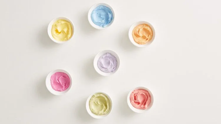 Martha Stewart all-natural tinted buttercream in seven small white bowls in yellow, blue, orange, purple, pink, green and red