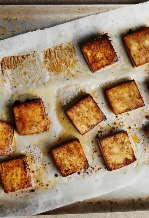Martha Stewart all-purpose baked tofu squares, crisp and golden brown, on a parchment-lined baking sheet