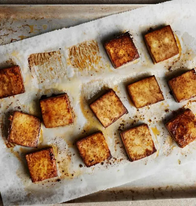 Martha Stewart all-purpose baked tofu squares, crisp and golden brown, on a parchment-lined baking sheet
