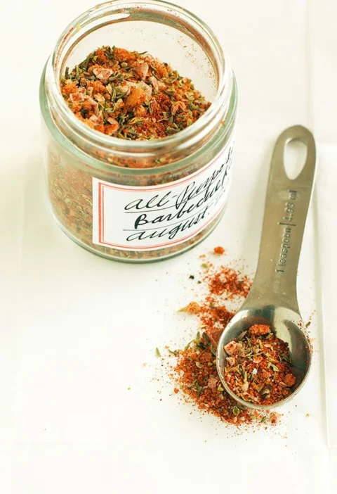 Martha Stewart all-purpose spice rub in a labeled glass jar next to a measuring spoon of the red-orange herb and spice mix