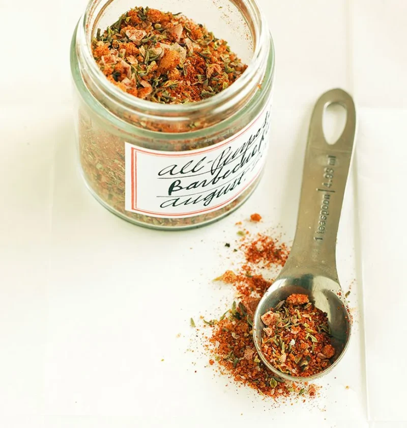 Martha Stewart all-purpose spice rub in a labeled glass jar next to a measuring spoon of the red-orange herb and spice mix