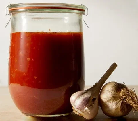 Martha Stewart all-purpose tomato sauce in a glass jar next to two heads of garlic on a wooden surface