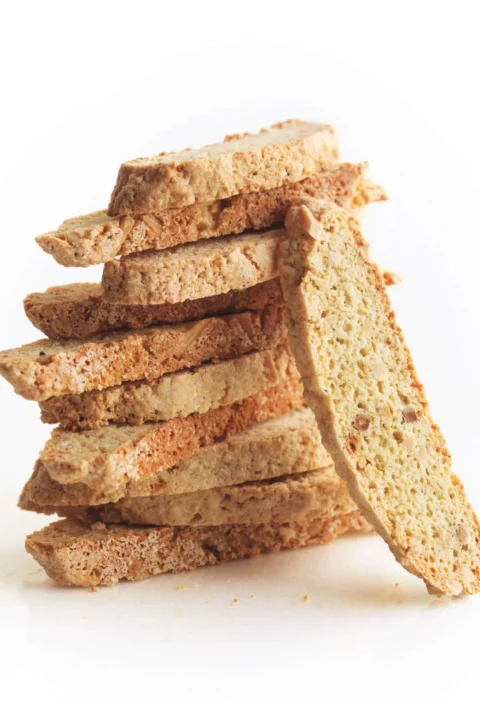 Stack of crisp almond biscotti slices with one slice leaning against the pile, showing slivered almonds in the crumb