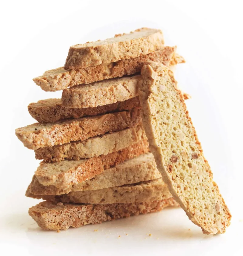 Stack of crisp almond biscotti slices with one slice leaning against the pile, showing slivered almonds in the crumb