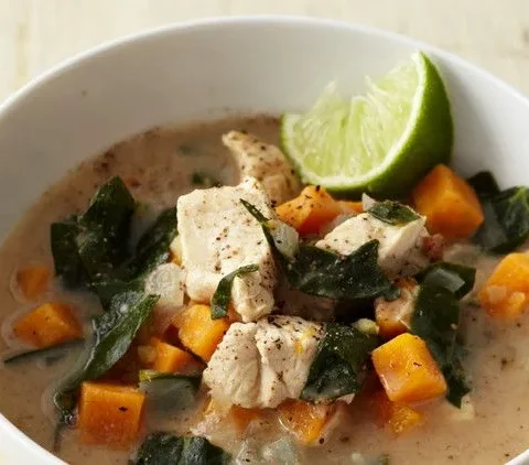 Martha Stewart almond chicken soup with sweet potato, collards and ginger in a white bowl with a lime wedge