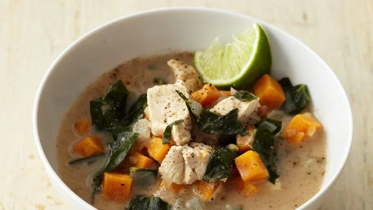 Martha Stewart almond chicken soup with sweet potato, collards and ginger in a white bowl with a lime wedge