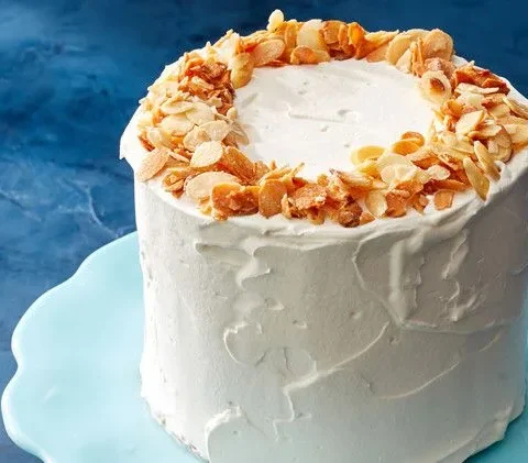 Martha Stewart almond-crunch ice cream cake frosted with whipped cream and topped with a ring of toasted sliced almonds on a pale blue cake stand