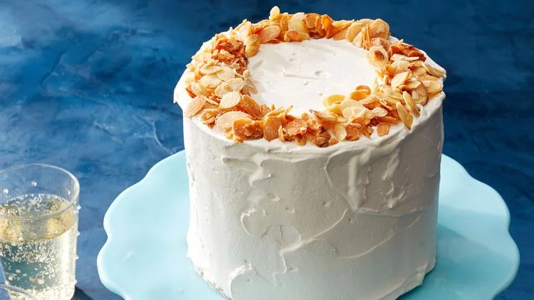 Martha Stewart almond-crunch ice cream cake frosted with whipped cream and topped with a ring of toasted sliced almonds on a pale blue cake stand
