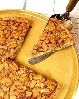 Martha Stewart almond tart with golden sliced almond topping, one slice lifted on a server from a yellow plate