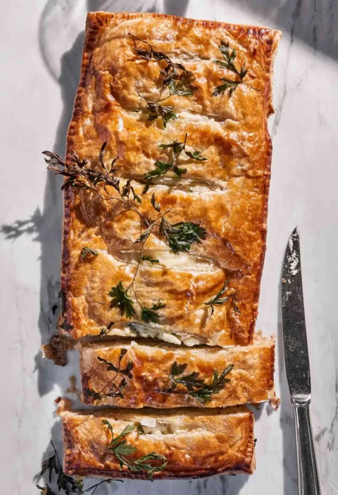 Martha Stewart Alsatian potato pie, a golden puff pastry pie topped with parsley sprigs, sliced on a marble surface
