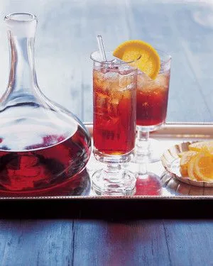 Martha Stewart Americano cocktail in a tall glass with ice and an orange slice next to a glass carafe on a silver tray