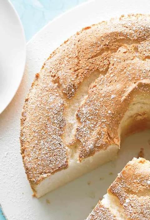 Martha Stewart angel food cake with a golden dusted top, one slice cut out and served on a small white plate