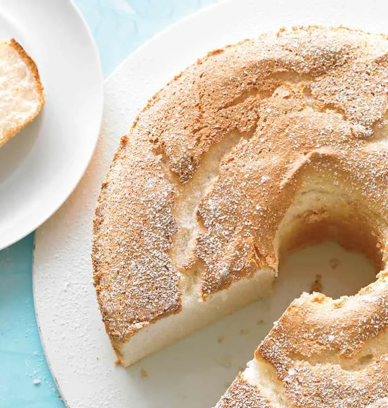 Martha Stewart angel food cake with a golden dusted top, one slice cut out and served on a small white plate