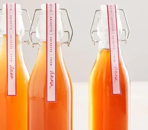Three swing-top glass bottles of Martha Stewart anisette liqueur with pink anisette gift labels