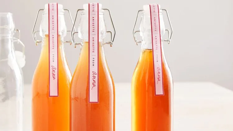 Three swing-top glass bottles of Martha Stewart anisette liqueur with pink anisette gift labels